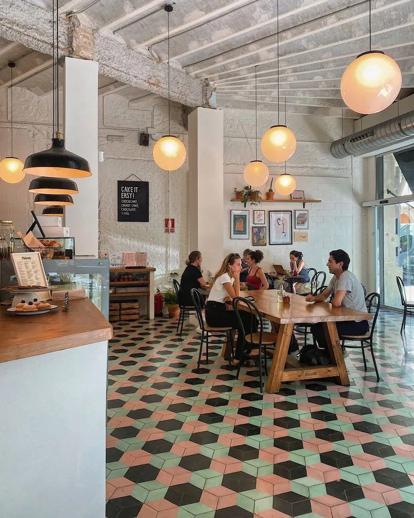 L’interior de La Malcriada, amb el terra de rajoles hexagonals roses, verdes i negres, llums de globus i clients dinant a la taula llarga