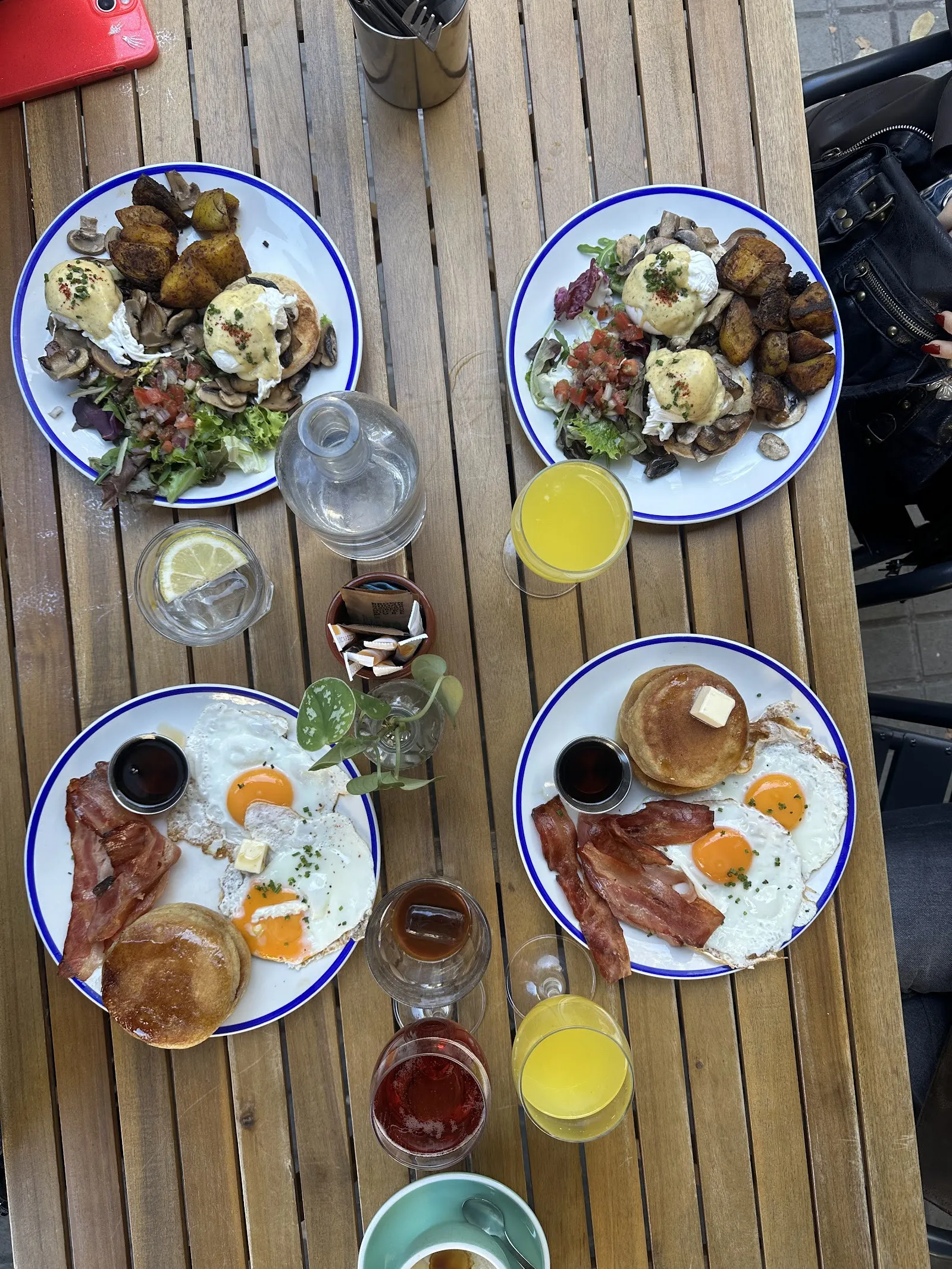 Una taula de la terrassa plena d’esmorzars: ous, tortites, bacon i sucs
